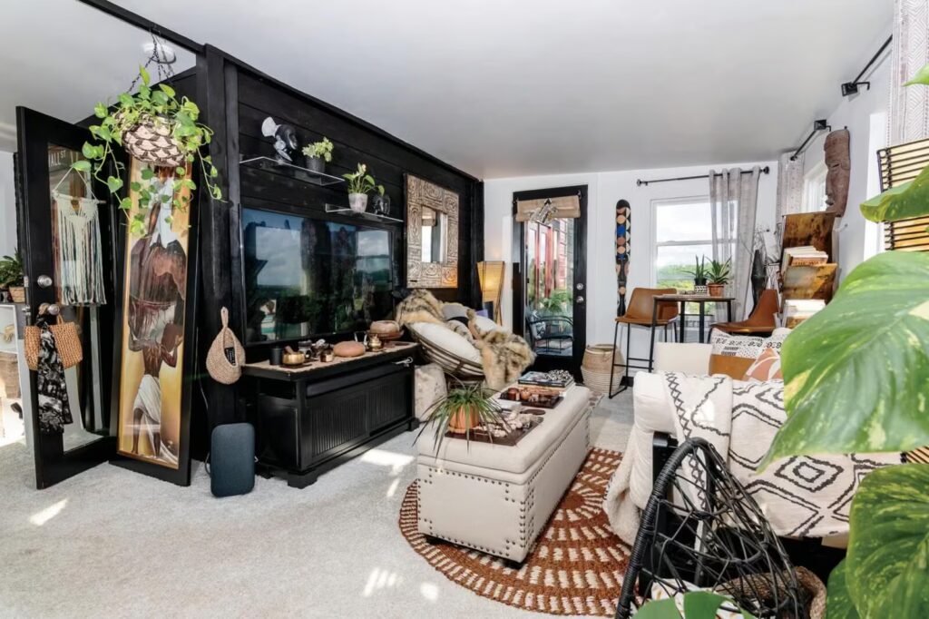 Prostrani dnevni boravak u boemskoj kućici koji je opremljen kaučem na razvlačenje, stolom, komodom te mnoštvom ukrasnih predmeta i biljaka