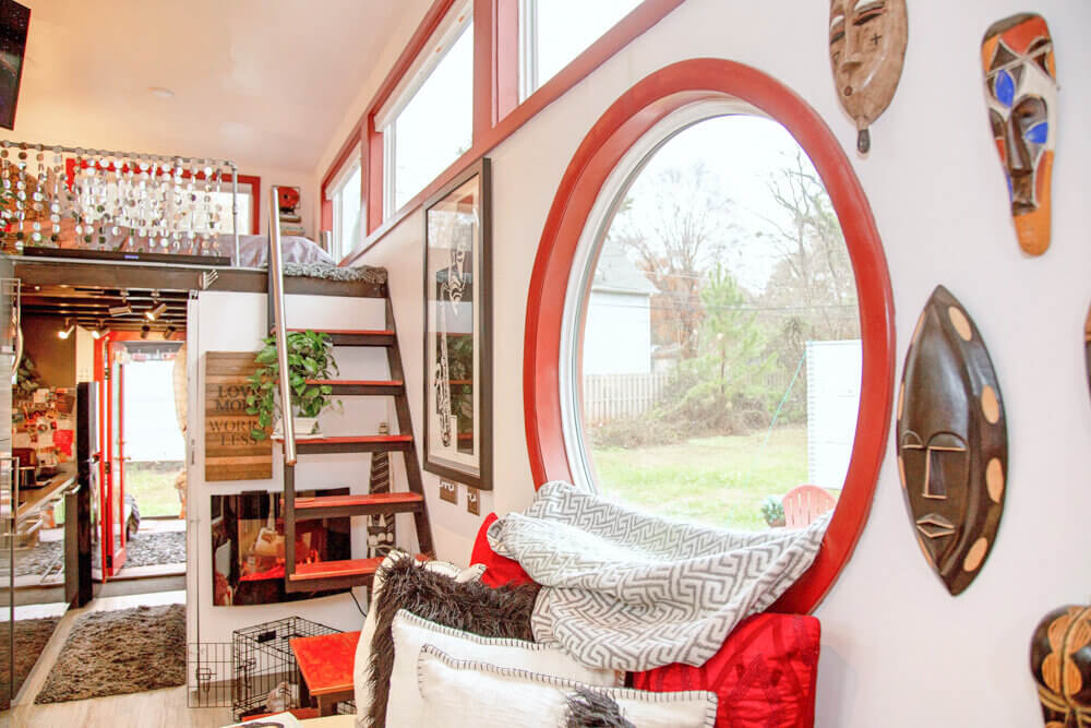 Dnevni boravak boemske kućice u crveno-bijelom tonu s fokusom na okrugli prozor koji gleda na dvorište