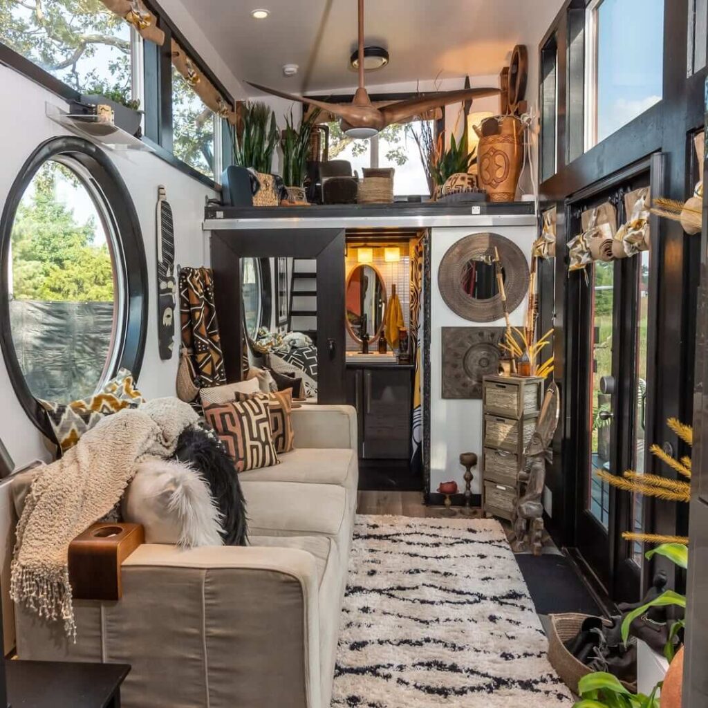 Dnevni boravak boemske kućice u kojem se nalazi svijetli kauč, svijetli tepih sa tamnim šarama te nekoliko ukrasnih predmeta i biljaka