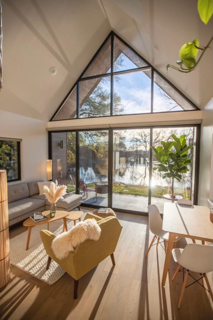 Prostrana, moderna soba u kućici s udobnim namještajem i modernim dizajnom interijera te velikim staklenim stijenama koje nude prekrasan pogled na jezero i šumu