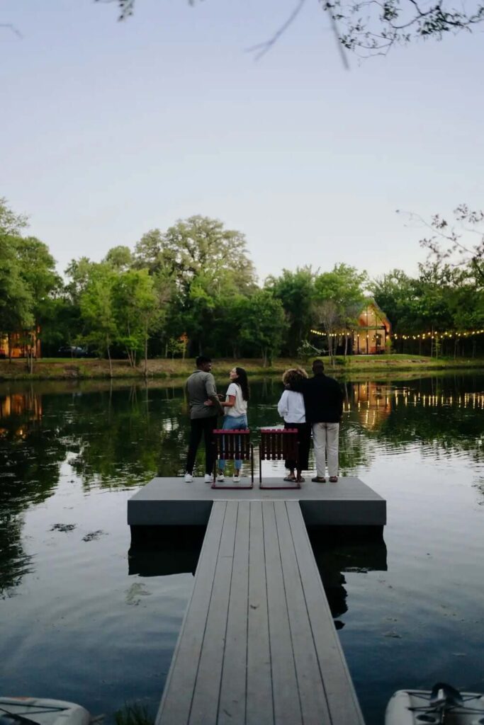 Jezero okruženo drvećem, s platformom na vodi na kojoj se nalaze dvije stolice ispred kojih stoji dva zaljubljena para.