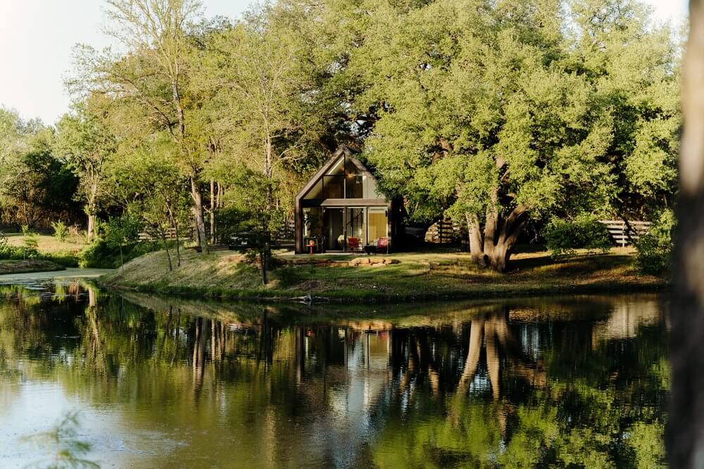 Kućica s velikim staklenim prozorima, smještena uz jezero. Kućica se zrcali u vodi, a okolo nje je šuma