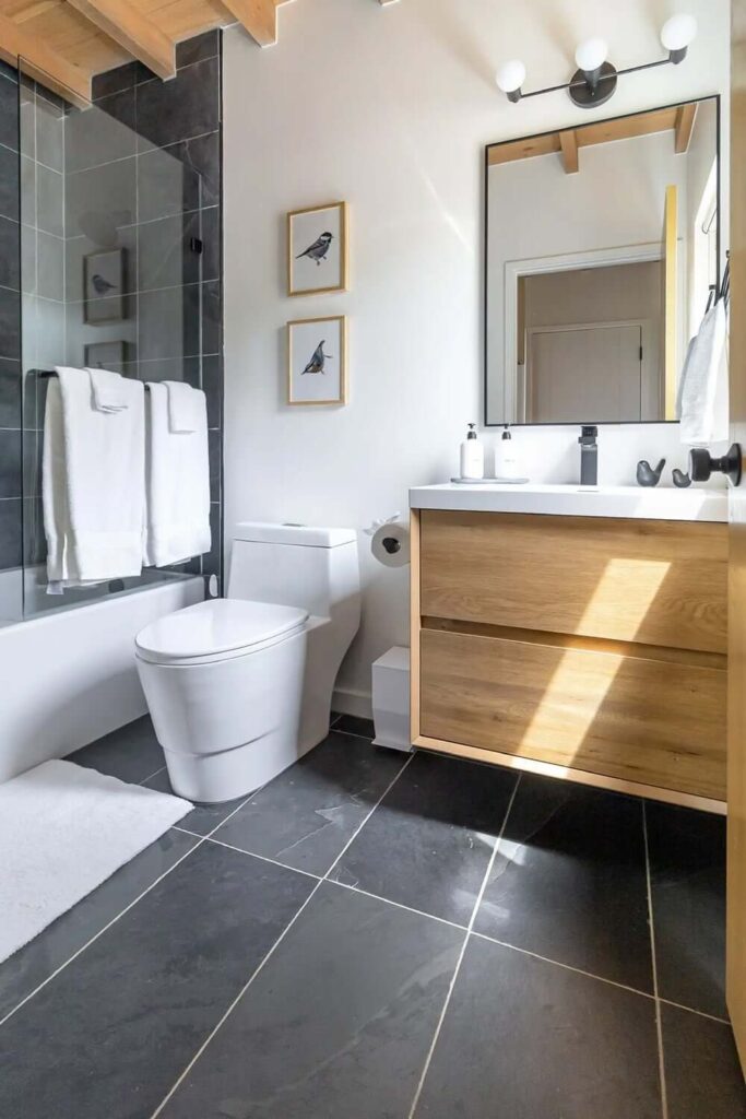 Moderna kupaonica unutar kućice s crnim pločicama, tuš kabinom, WC školjkom i umivaonikom