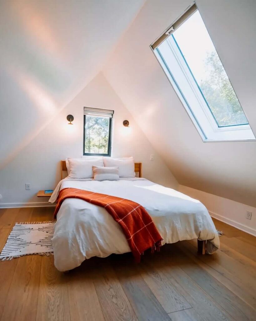 Soba u potkrovlju kućice s kosim stropom, prozorom i drvenim podom. U sobi se nalazi krevet s bijelom posteljinom i dva mala noćna stolića
