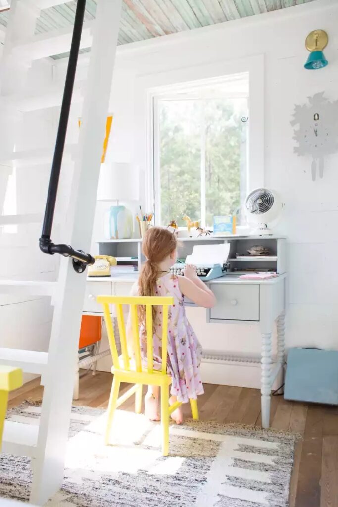 Djevojčica sjedi na žutoj stolici i piše na pisaćem stroju na bijelom radnom stolu