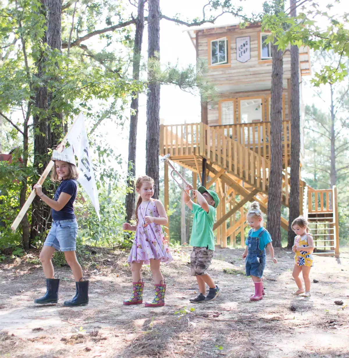 Djeca u igri ispred drvene kućice na drvetu, okruženi šumom i prirodom