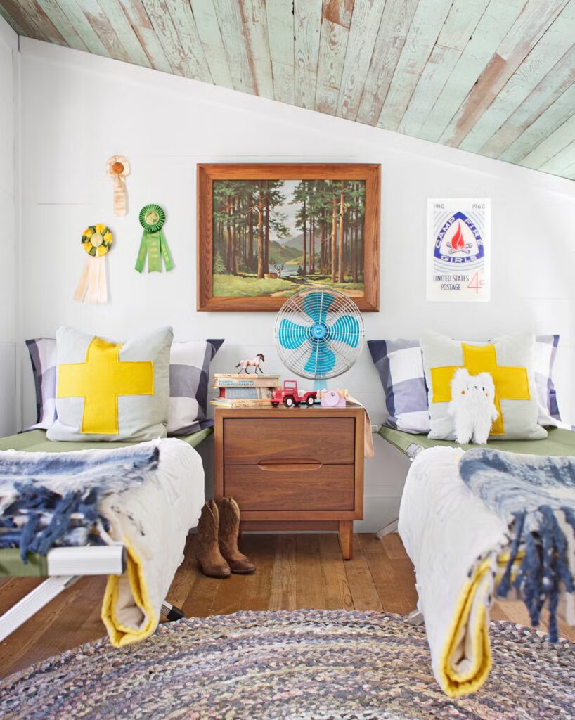 Dva dječja kreveta sa šarenom posteljinom i drveni noćni ormarić između njih