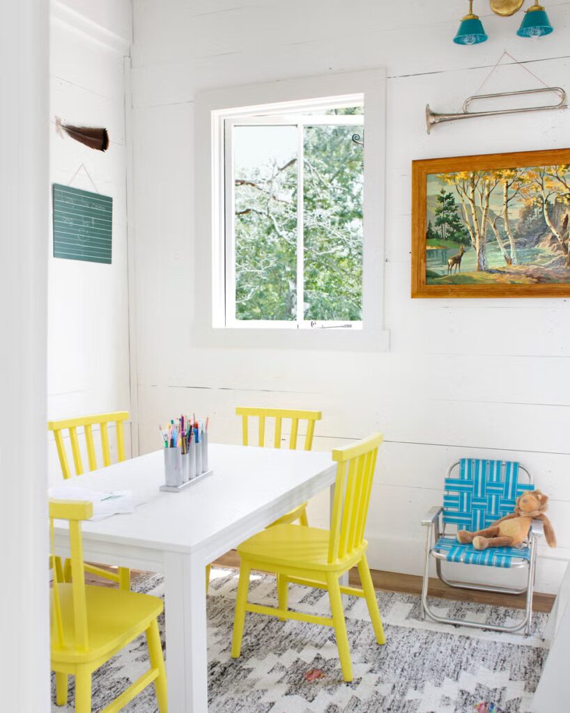 Bijeli stol za crtanje sa žutim stolicama u kućici na drvetu