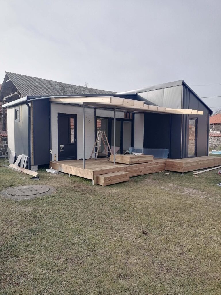 Moderna modularna kućica sa drvenom terasom i pergolom u izgradnji, na travnjaku