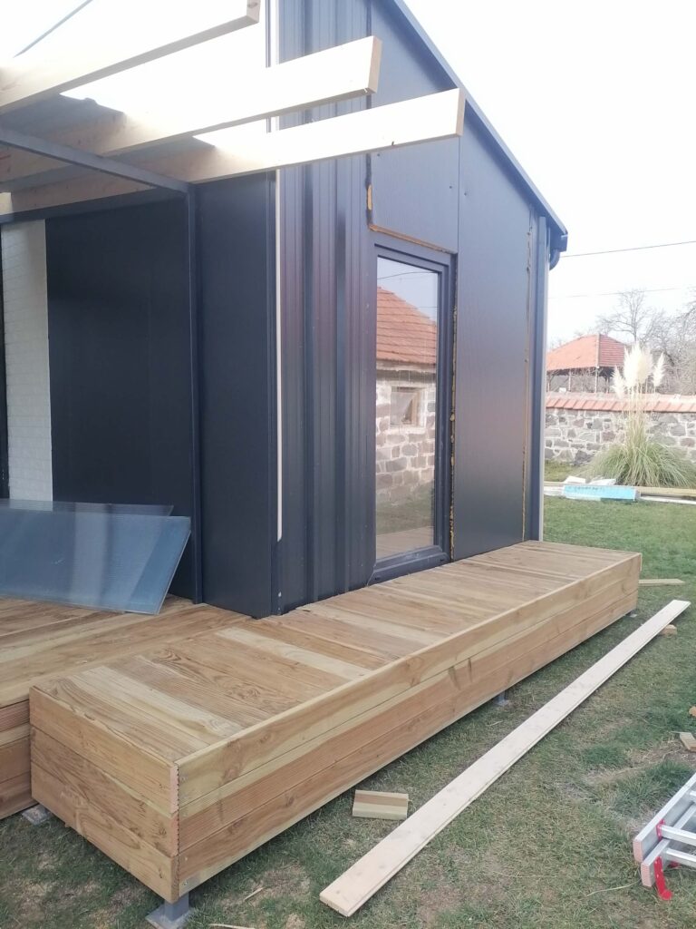 Detalj moderne modularne kućice sa drvenom terasom i pergolom u izgradnji na travnjaku