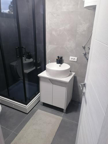 Kupaonica s modernom crnom tuš kabinom, bijelim umivaonikom, te sivim pločicama