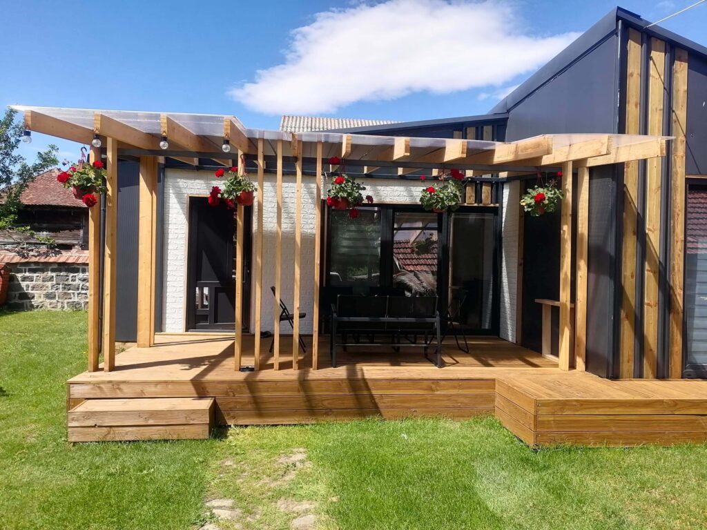 Moderna modularna kuća s drvenom terasom, pergolom, visećim cvijećem i vanjskim namještajem