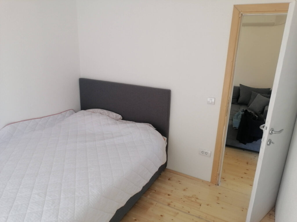 Spavaća soba s krevetom, sivim uzglavljem i bijelom posteljinom