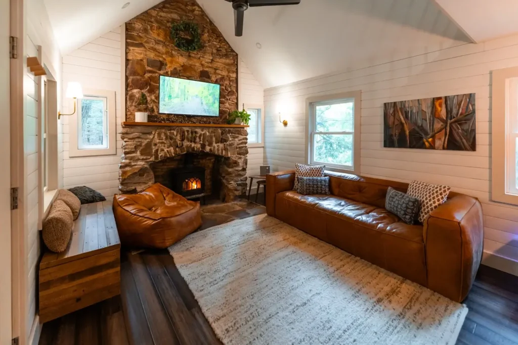 Dnevni boravak u kolibi s kamenim kaminom, kožnim kaučem, televizorom i drvenim zidovima