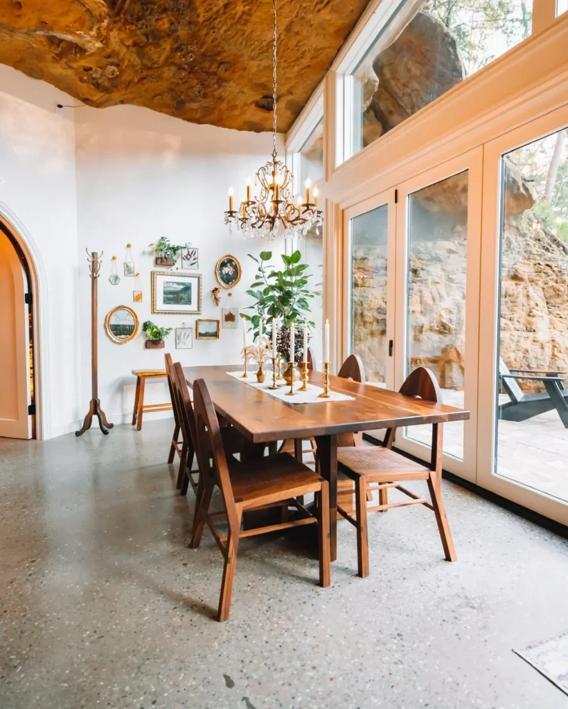 Blagovaonica s drvenim stolom i stolicama, staklenim stijenama, visokim kamenim stropom i lusterom