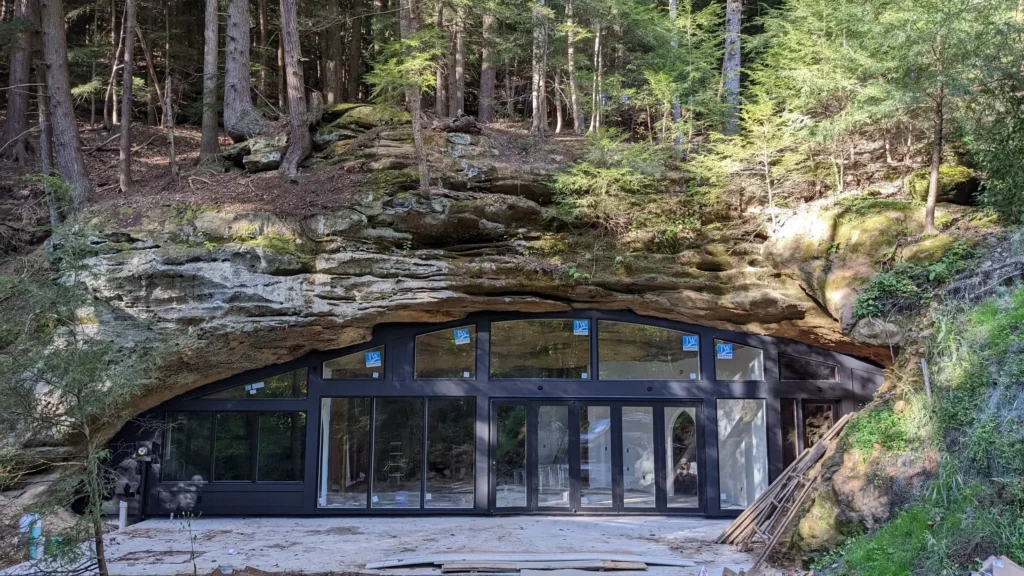 Suvremena kuća u špilji u izgradnji, s velikim staklenim prozorima ugrađenim u stijenu okruženu drvećem