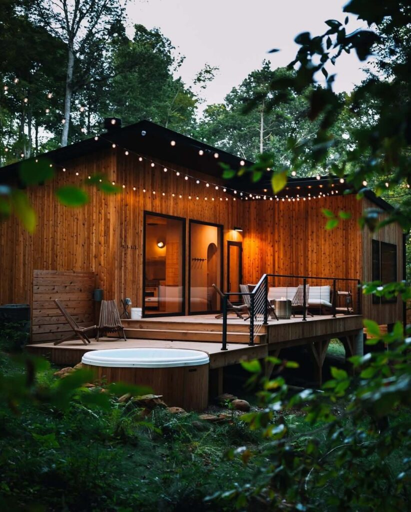 Drveni bungalov s terasom i hidromasažnom kadom, okružen šumom i ukrasnom rasvjetom