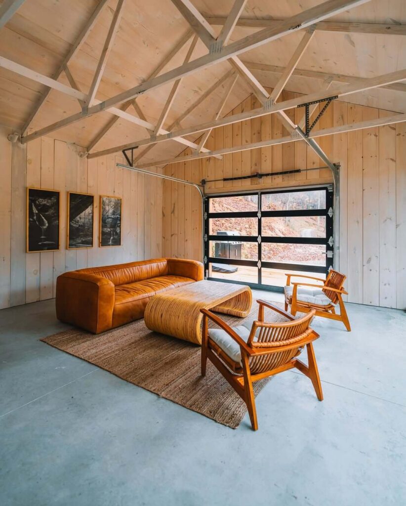 Svijetla prostorija s kožnim kaučem, drvenim stolicama i industrijskim vratima s prozorima