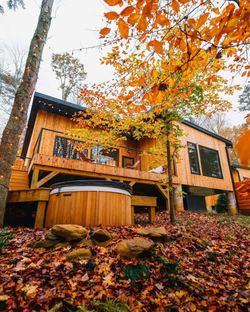 Drveni bungalov za odmor u jesen, sa hidromasažnom kadom i narandžasto-žutim lišćem na tlu i drveću