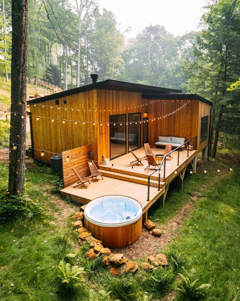 Moderni drveni bungalov s velikom terasom, rasvjetom i drvenom hidromasažnom kadom u šumi