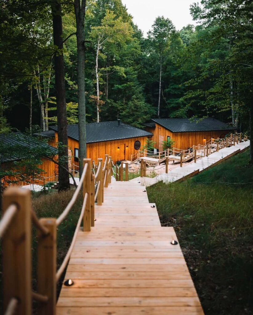 Drvena staza sa svjetlima koja vodi nizbrdo do drvenih bungalova u šumi