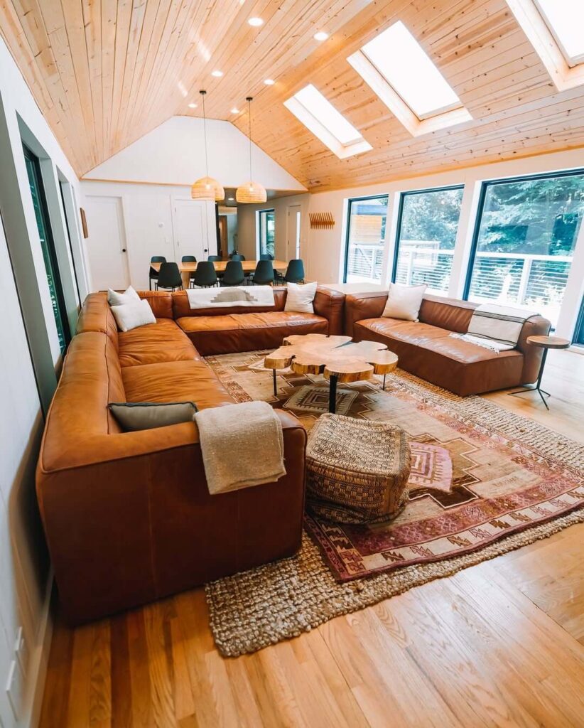 Prostrani dnevni boravak s kožnim kutnim garniturama, drvenim stropom i velikim prozorima
