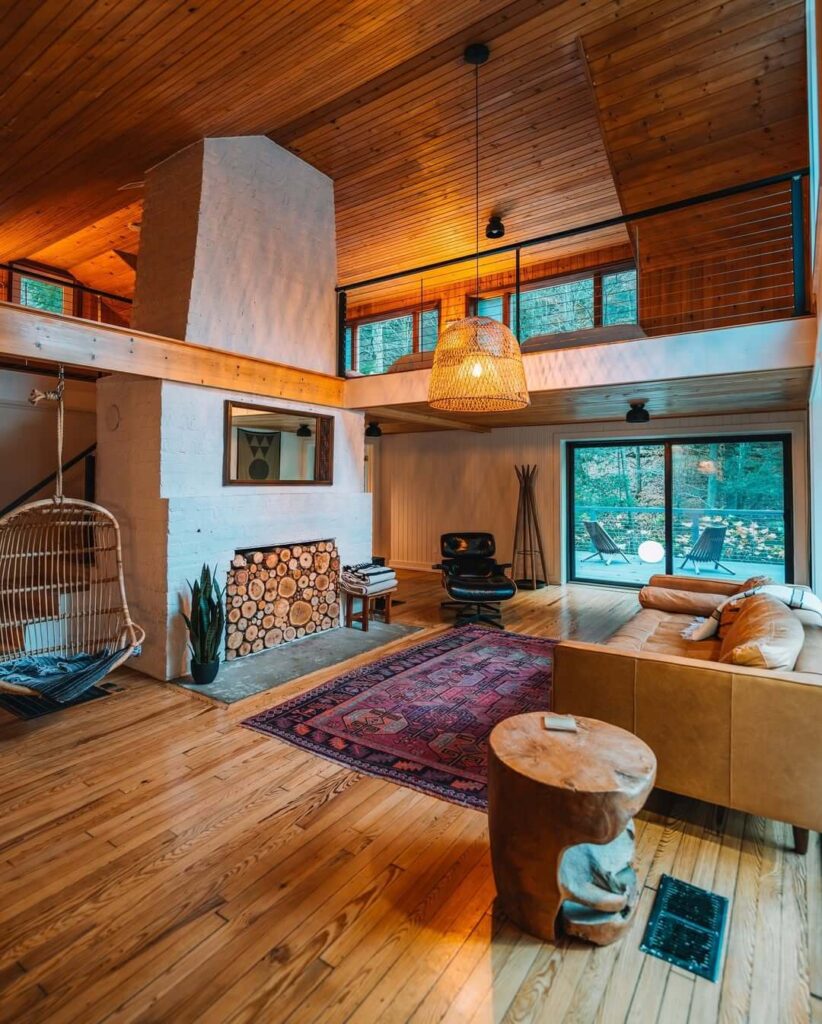 Prostrani dnevni boravak s drvenim podovima i stropom, kaminom, pletenom ljuljačkom i terasom