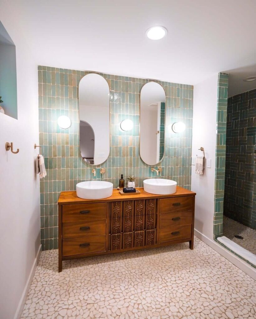 Moderna kupaonica s pločicama u boji mente, drvenim ormarićem s dvostrukim umivaonicima i ovalnim zrcalima