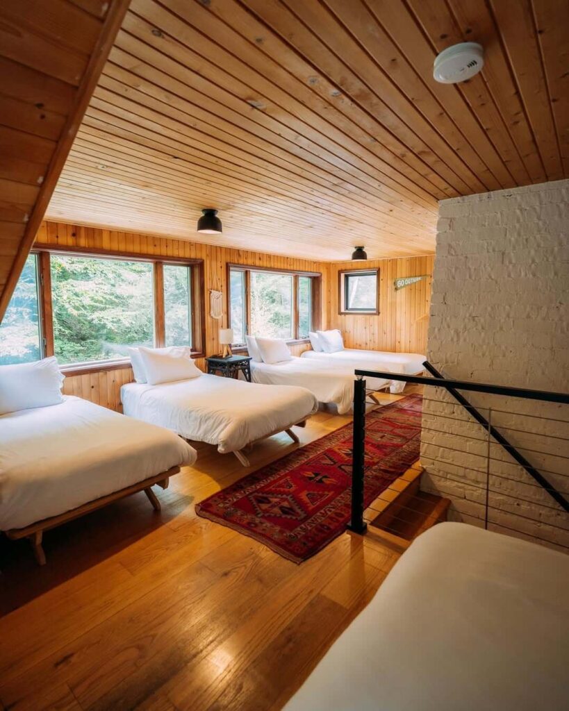 Spavaonica na tavanu s drvenim zidovima i stropom, četiri kreveta i velikim prozorima