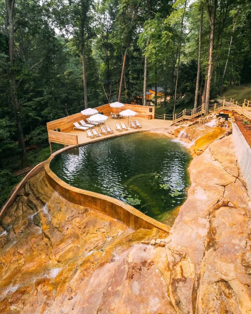 Prirodni bazen okružen kamenom i šumom, s drvenim sunčalištem