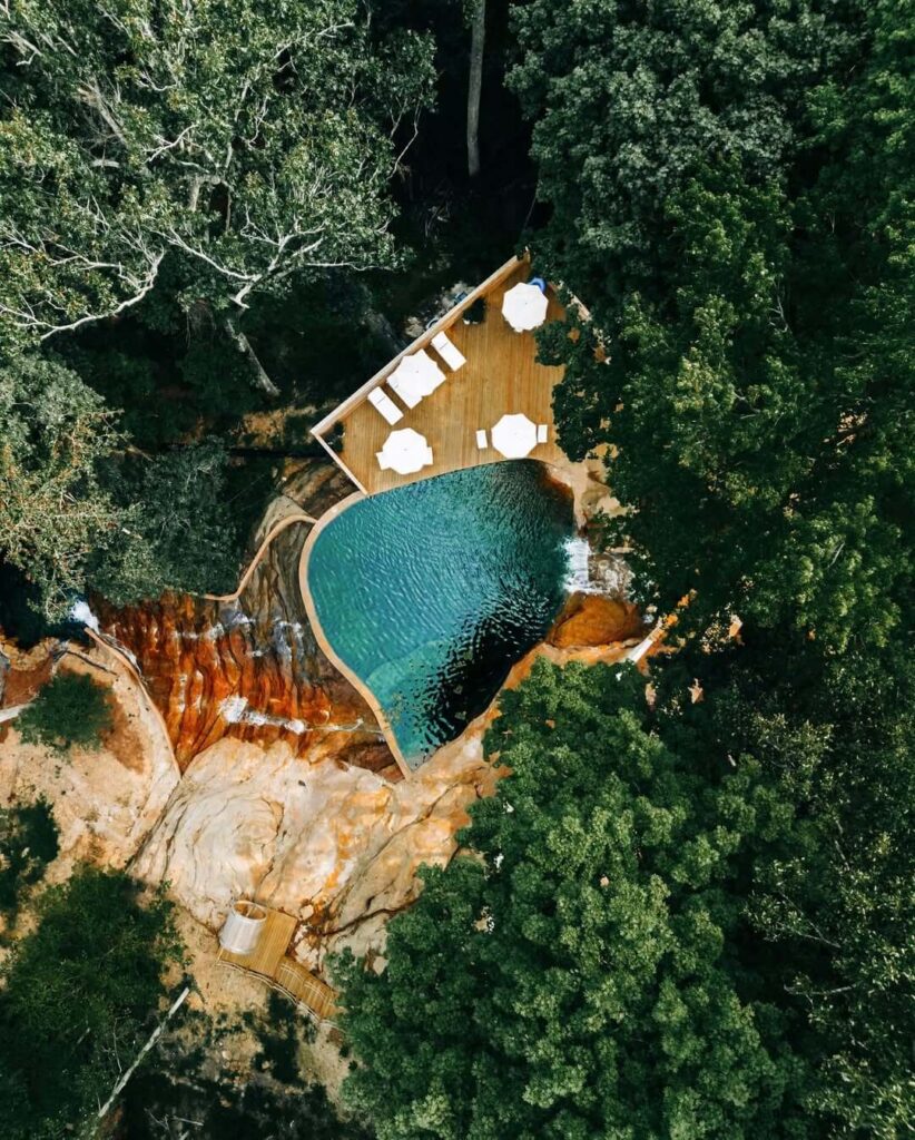 Pogled iz zraka na prirodni bazen u obliku srca s terasom, okružen gustom šumom