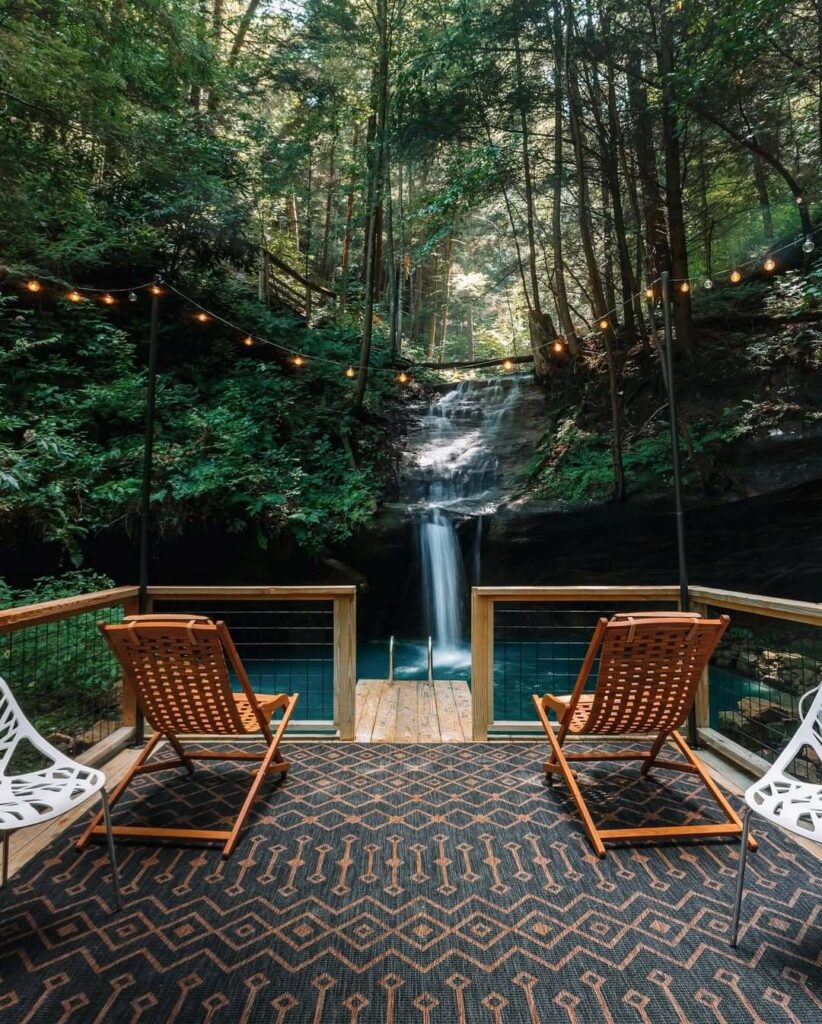Terasa s ležaljkama i uzorkovanim tepihom, s pogledom na prirodni bazen i vodopad u šumi