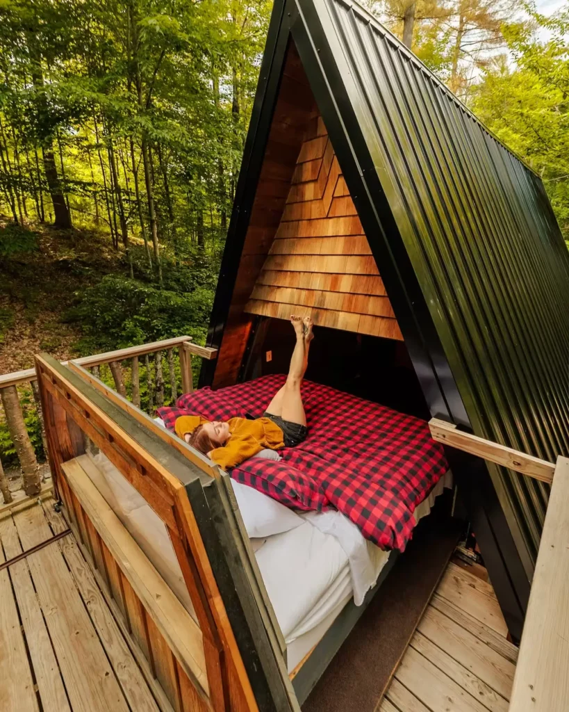 Djevojka leži na krevetu koji je izvučen iz A-frame kućice izravno na balkon u prirodi