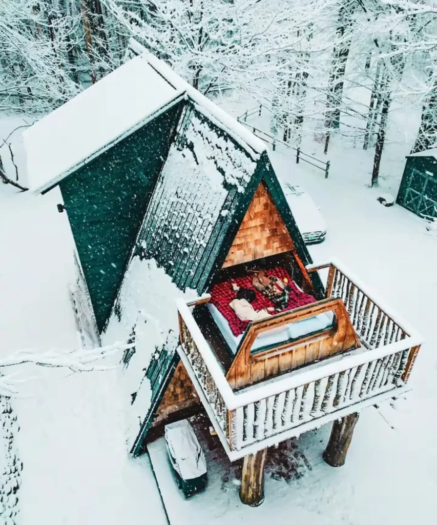 Pogled iz zraka na krevet izvučen na balkon drvene A-frame kućice prekrivene snijegom
