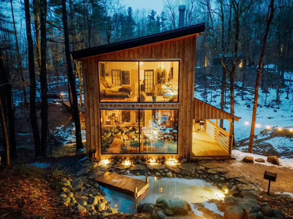 Osvijetljena dvoetažna drvena koliba s velikim staklenim stijenama uz jezerce u sumrak