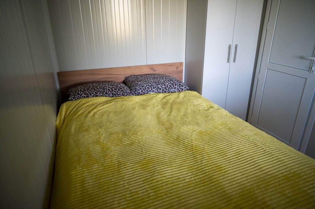 Spavaća soba s bračnim krevetom, žutom dekom, jastucima leopard uzorka i bijelim ormarom